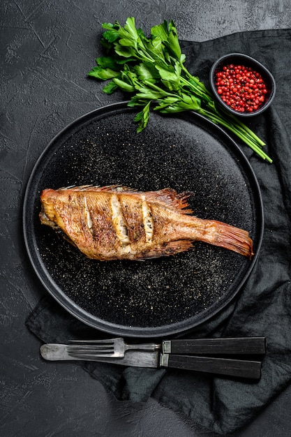 Sea perch fried served on a round plate with parsley  Black surface    surface