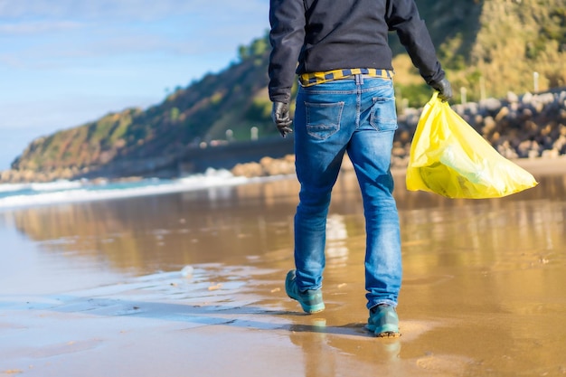 Sea pollution unrecognizable person walking on the beach\
collecting plastics ecology concept