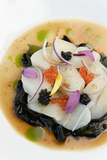 Sea salad with scallops and red caviar on a white plate Restaurant dish closeup