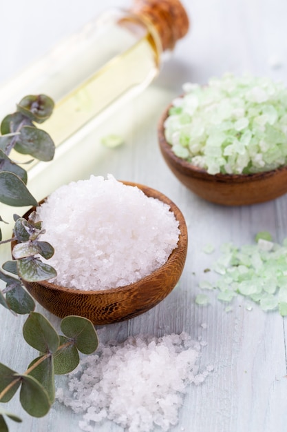 Sea salt in bowl, aroma oil in bottles, Wellness and flowers on grey surface and flowers on vintage wooden table. Selective focus.