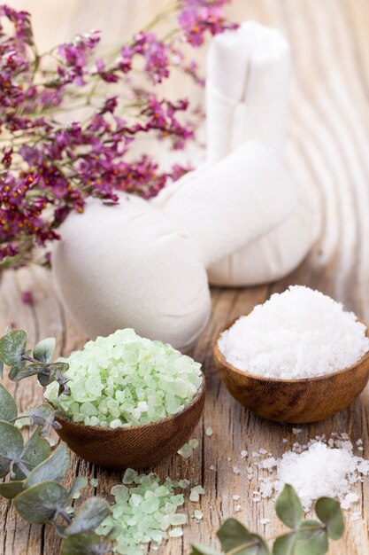 Photo sea salt in bowl, aroma oil in bottles, wellness and flowers on grey textured and flowers on vintage wooden. selective focus.