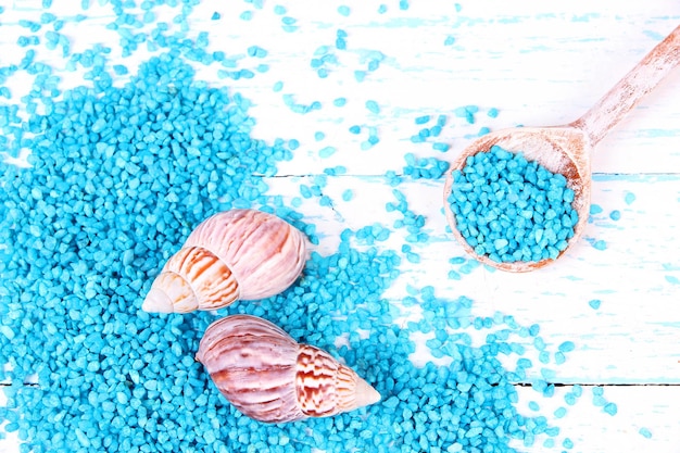 Sea salt crystals in wooden spoons with sea shells on color wooden background