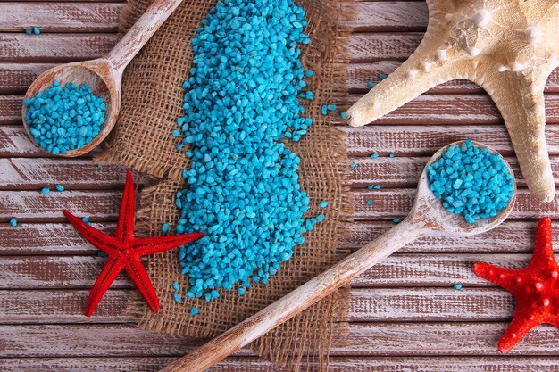 Sea salt crystals in wooden spoons with starfish on color wooden background