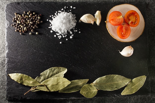 Sea salt pepper cherry tomatoes and bay leaf on black rustic slate stone background