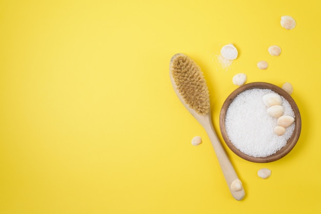 Sea salt and a stiff body brush on a yellow background. home skin care for cellulite. concept skin care in spring, home Spa, care products