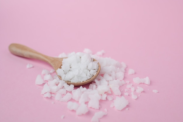 Sea salt in a wooden spoon on pink background