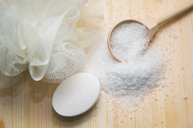 Sea salt in wooden spoon, soap, sponge on wood