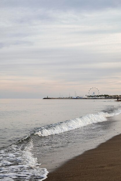 Foto paesaggio marino onde che si rompono sulla biforcazione di una spiaggia un piccolo porto con una ruota panoramica
