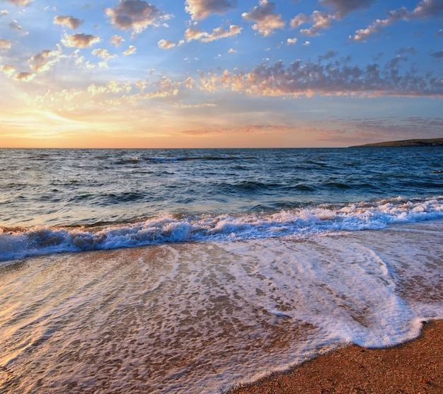 Sea surf wave break on sunset sandy coastline