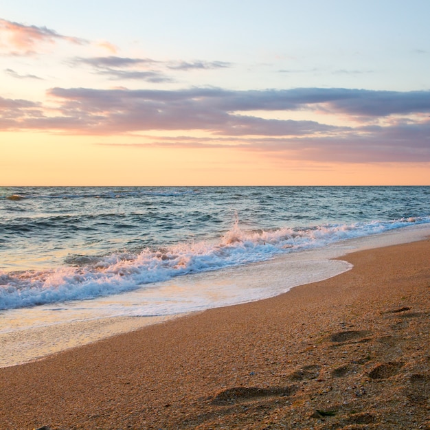 Sea surf wave break on sunset sandy coastline