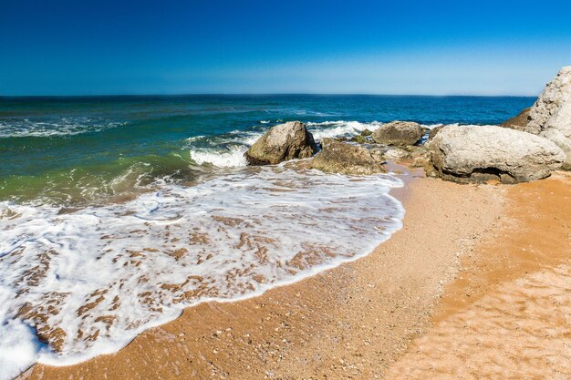 岩のある砂浜に白い泡を持つ海の波