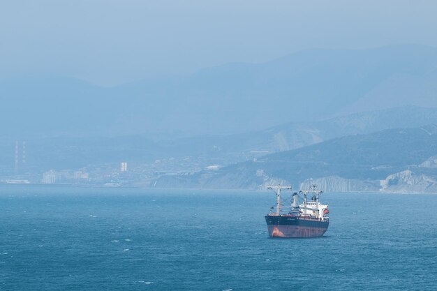 Sea tanker barge ship in sea in distance calm water sunshine and sun calm seascape in distance mountains and fog