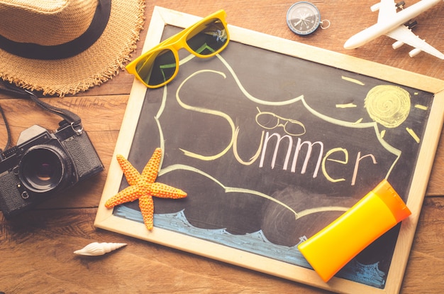 sea travel accessories a hat, sunglasses, camera. placed on wooden with word 'summer