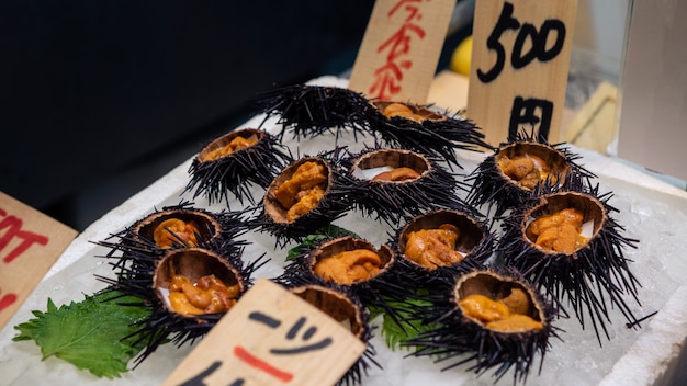 Photo sea urchins sashimi fresh open and ready to eat on ice in kyoto fish market. close up of delicious traditional japanese uni seafood at stall for sale. japan food travel and cuisine store street snack