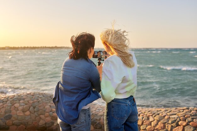 Женщины, отдыхающие на море, смотрят на экран смартфона, совершают онлайн-видеозвонок