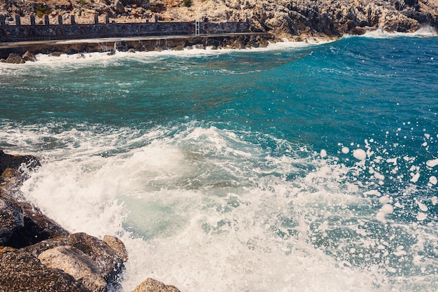 Sea water beats against rocky rocks and makes waves with foam rugged pier in the sea