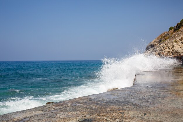 Морская вода бьется о скалы и образует волны пеной.