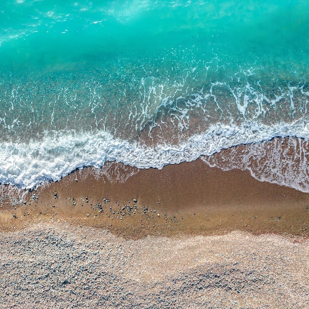 Sea waves over sand and pebbles beach, square shot, top view directly above