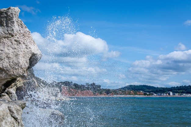 Sea waves splashing on rocks against sky