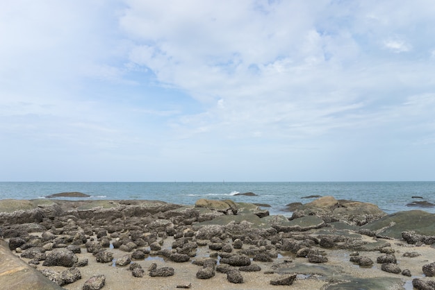 The sea with rocky beach is below the light blue sky. 