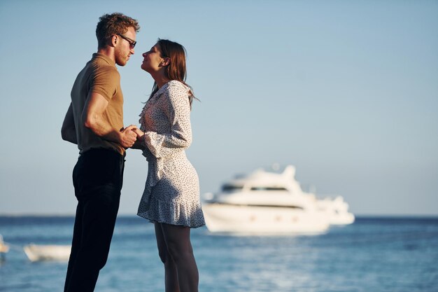 Sea and yacht at background Happy young couple is together on their vacation Outdoors at sunny daytime