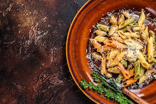 Seafood color Penne pasta in cream sauce on a plate. Dark background. Top view.  