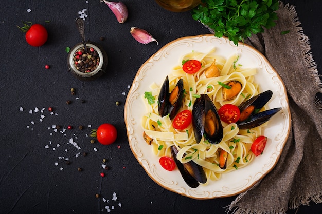 Seafood fettuccine pasta with mussels over black background. Mediterranean delicacy food. 