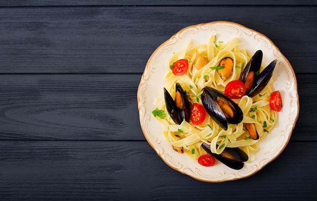 Seafood fettuccine pasta with mussels over black table. Mediterranean delicacy food. Flat lay. Top view