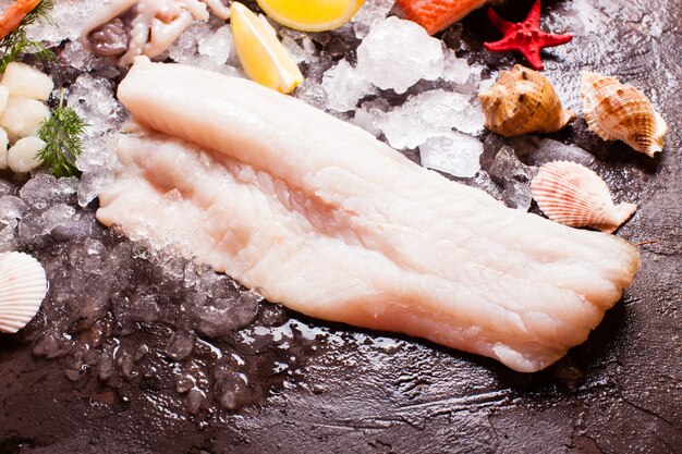 Seafood on the ice, cod fillets close up on the brown slate background