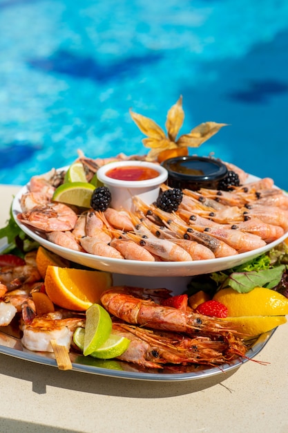 Морепродукты на роскошном курорте с видом на бассейн Креветки, омары, крабы, фруктовый соус из журавля