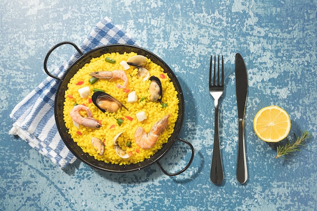 Foto paella di pesce sulla tradizionale padella per paella su sfondo blu rustico vista dall'alto