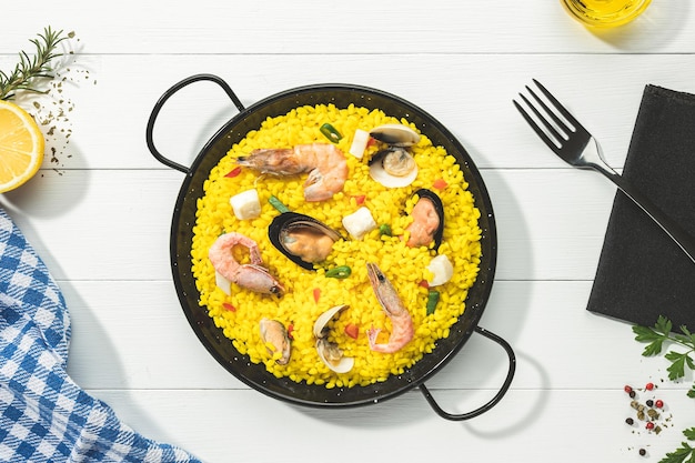 Foto paella di pesce sulla tradizionale padella per paella su base di legno bianco vista dall'alto