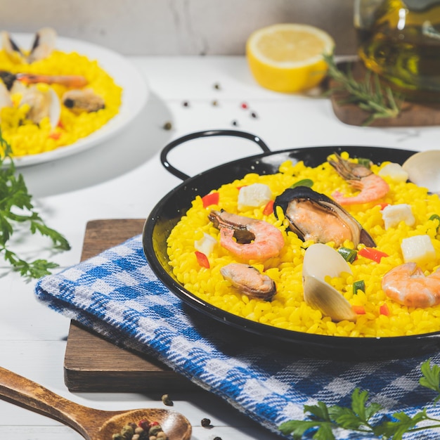 Photo seafood paella on traditional pan paella on white wood base square format