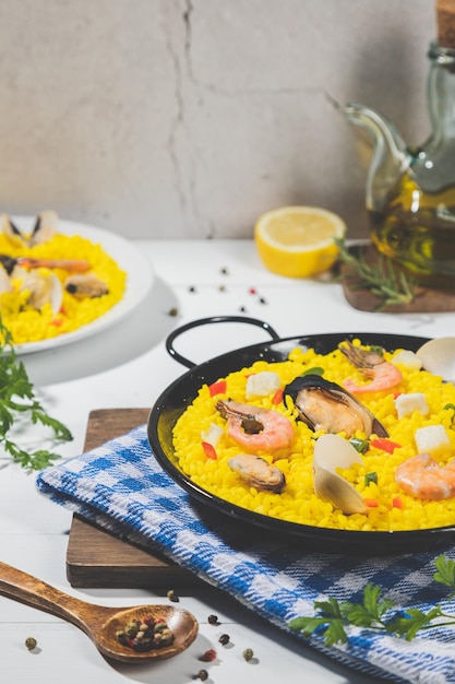 Foto paella di pesce su paella tradizionale in padella su base di legno bianco formato verticale