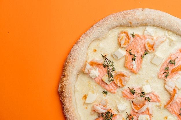 Seafood pizza combination of shrimp salmon with mozzarella cheese and gouda with feta on a creamy base Orange background top view Copy space