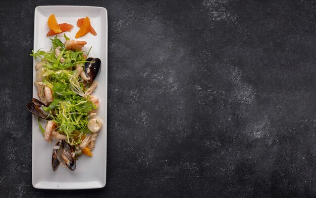 Seafood on a plate, mussels, scallop, shrimp, squid, with salad mix on a dark background