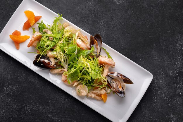 Seafood on a plate mussels scallop shrimp squid with salad mix on a dark background