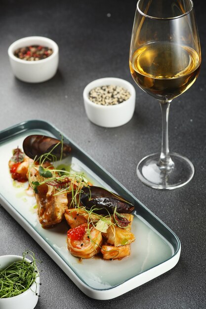 Seafood plate with mussels and shrimp toped microgreen closeup with glass of white wine.