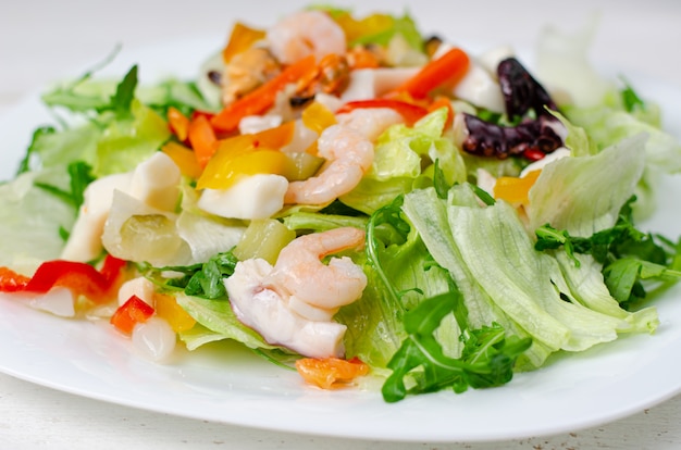 Салат из морепродуктов с овощами и листьями салата на белой тарелке