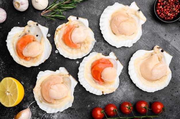 Seafood. Shellfish. Raw scallops with lemon set, on black dark stone table background, top view flat lay