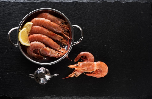 Seafood Uncooked Shrimps with lemon on Black Slate Background, top view