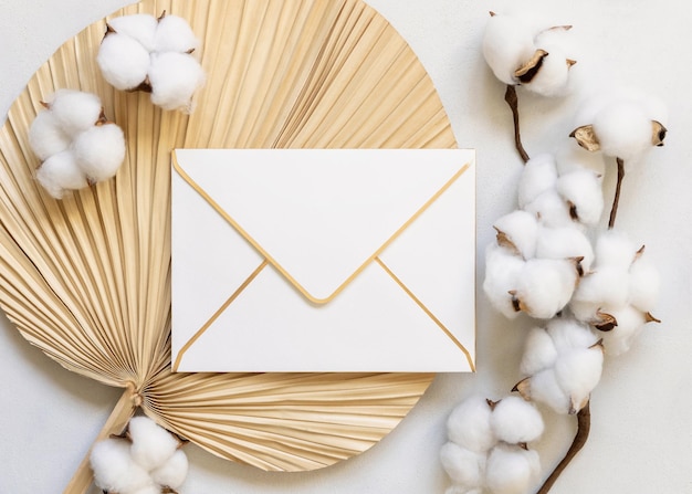 Sealed envelope on dried palm leaf with cotton flowers top view wedding mockup