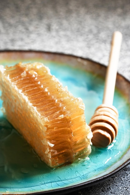 Sealed honeycomb of honey with wooden honey dipper  on a blue plate