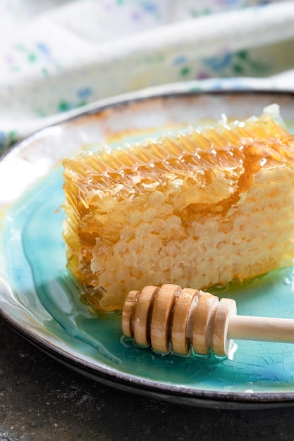 Sealed honeycomb of honey with wooden honey dipper for mixing and tasting natural honey on a blue po...