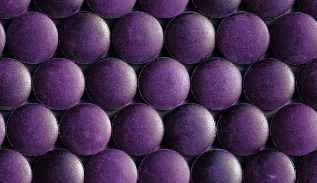 A seamless hexagonal pattern of many purple organic spirulina tablets laid tight in one layer on flat surface