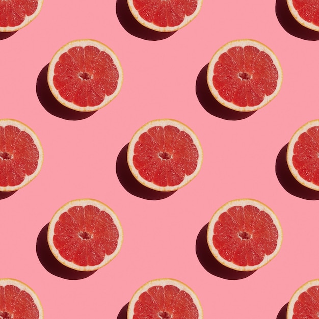 Seamless pattern of fresh ripe grapefruit with a shadow on a pink background