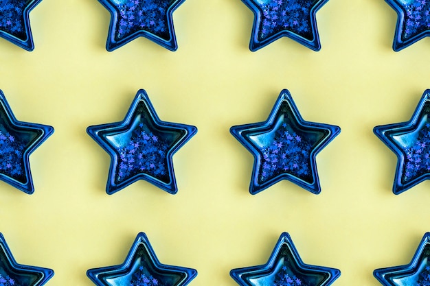 Seamless pattern from five pointed blue metallic star on yellow surface. Shining decoration.