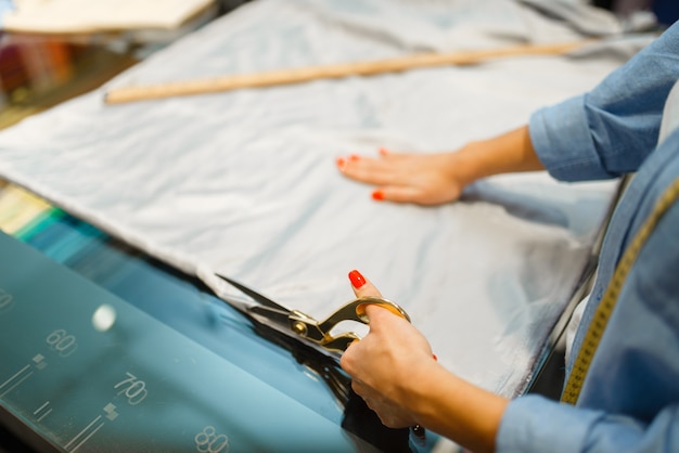 Photo seamstress cuts fabric with scissors in textile store. woman works with cloth for sewing, female tailor in workshop