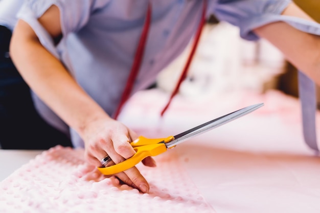 Швея-портниха разрезает ткань в своей мастерской по пошиву одежды