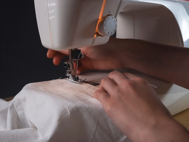 Руки швеи с тканью на швейной машине во время работы.